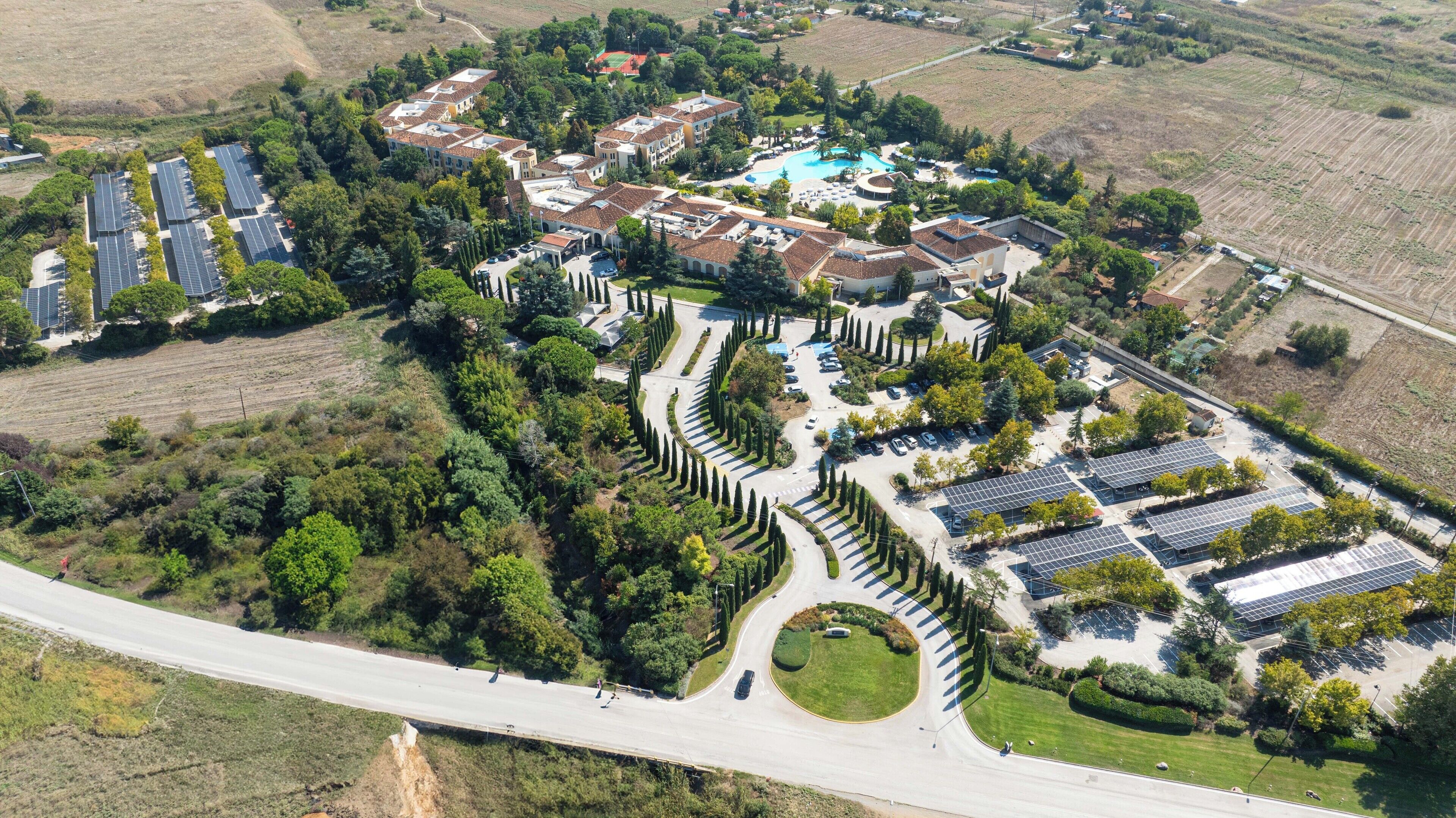 An aerial view of a residential area with solar panels, a swimming pool, and a winding road.