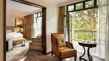 A hotel room with a large window, a leather armchair, a bed, a small table, and a luggage trolley.