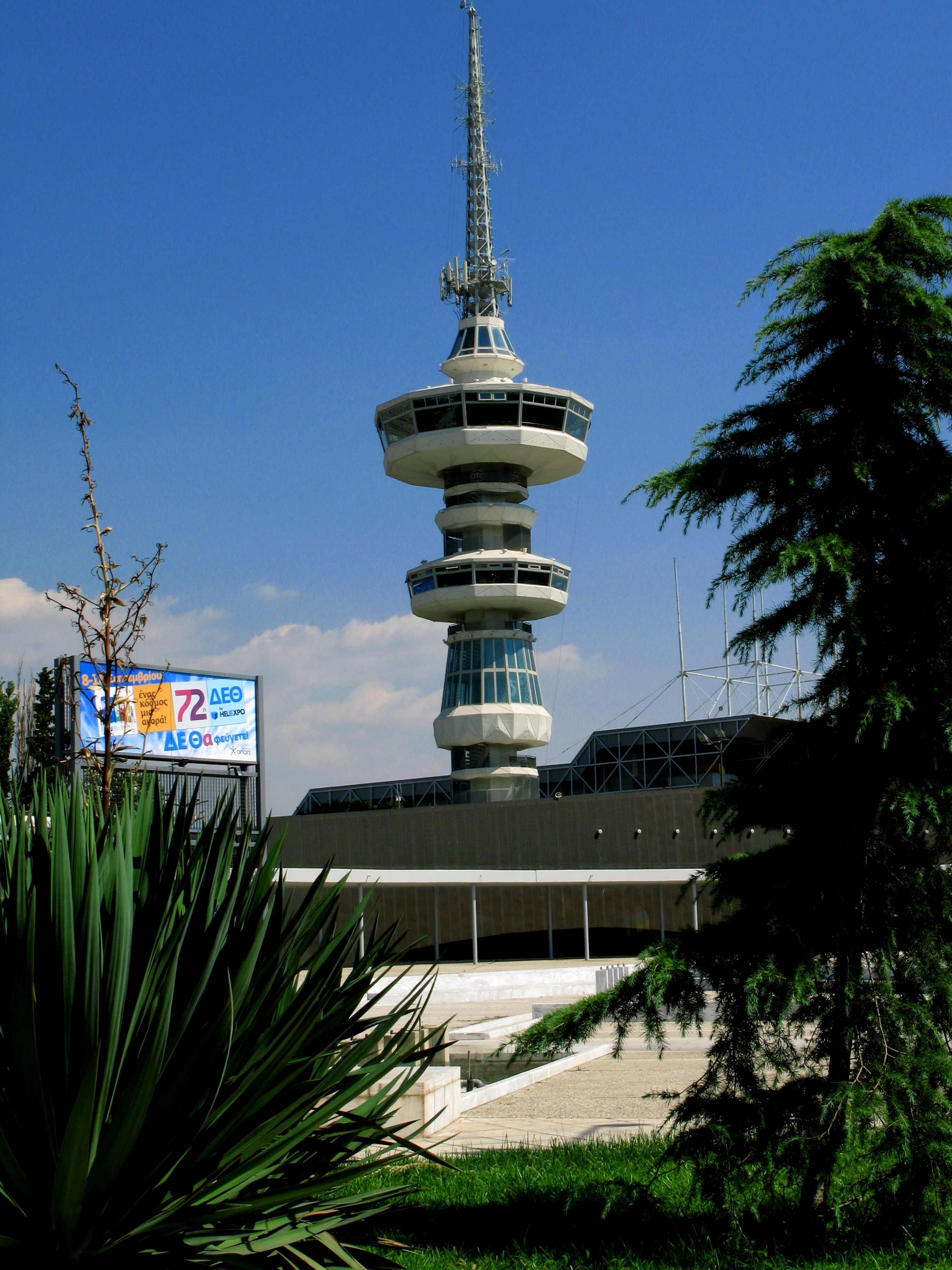 Una torre de varios niveles con diseño moderno, rodeada de vegetación y un cielo despejado.