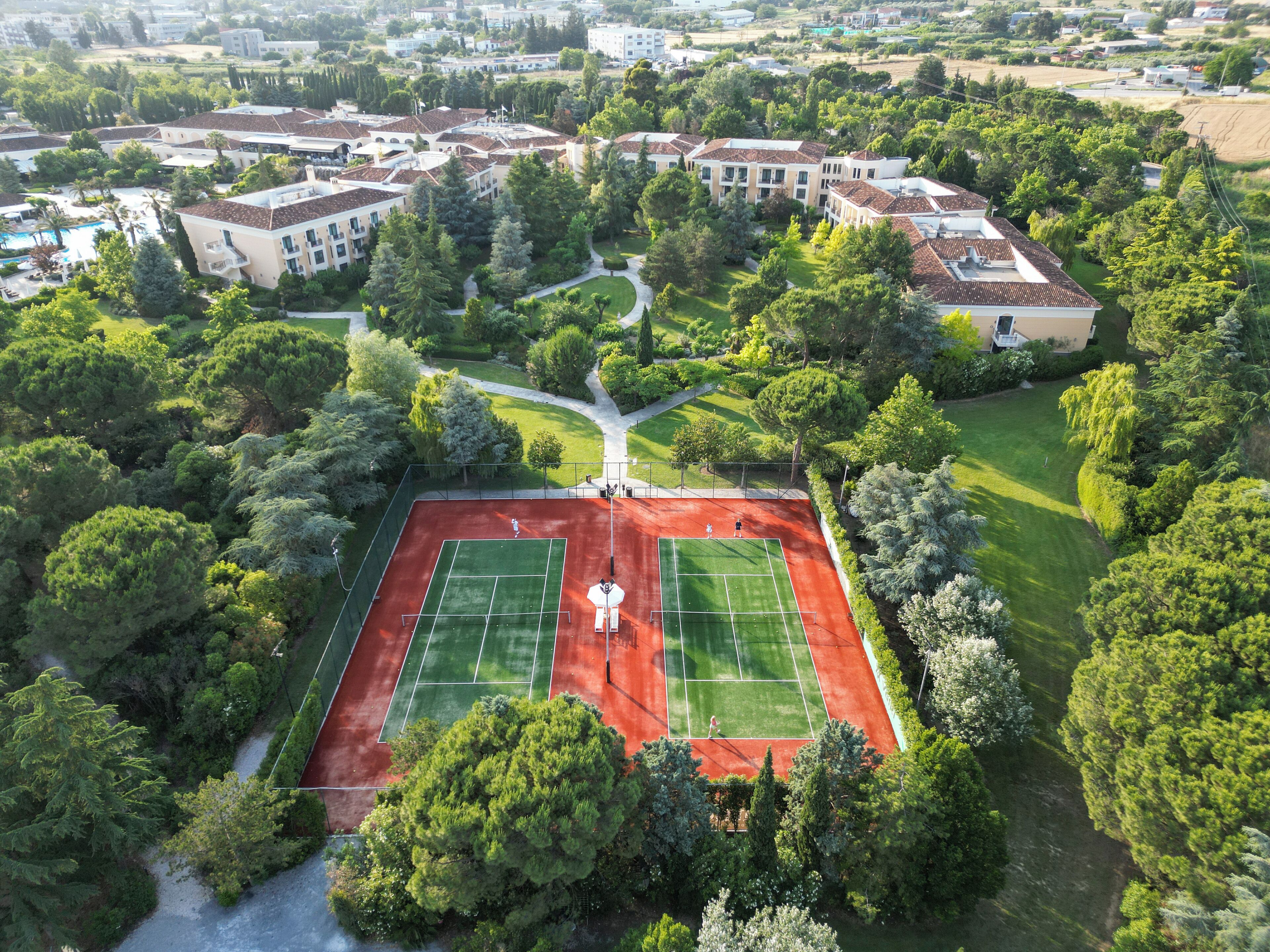 An aerial view of a residential area with a tennis court surrounded by lush greenery and a swimming pool.