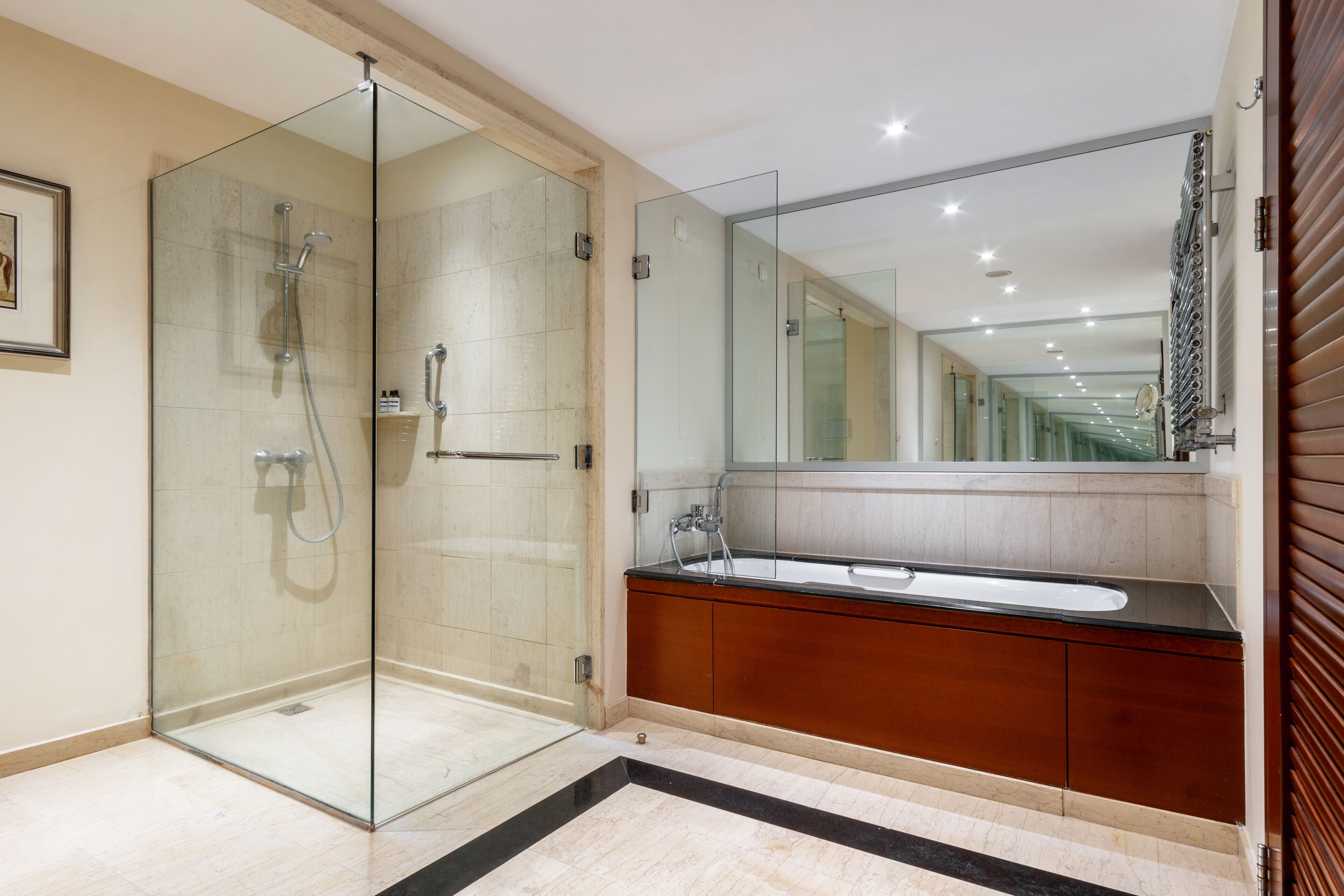A modern bathroom with a glass-enclosed shower, a large mirror, and a wooden vanity.