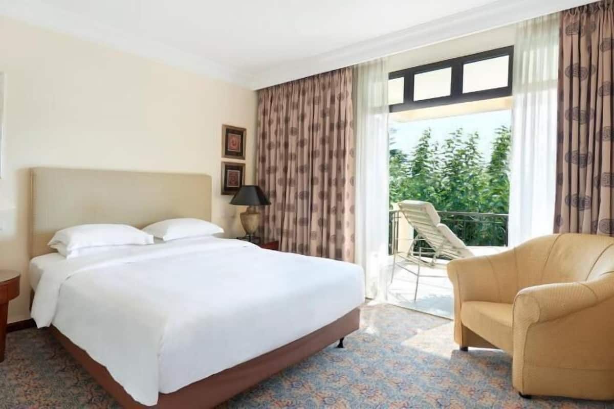 A hotel room with a bed, a chair, a nightstand, a lamp, and a window with curtains.