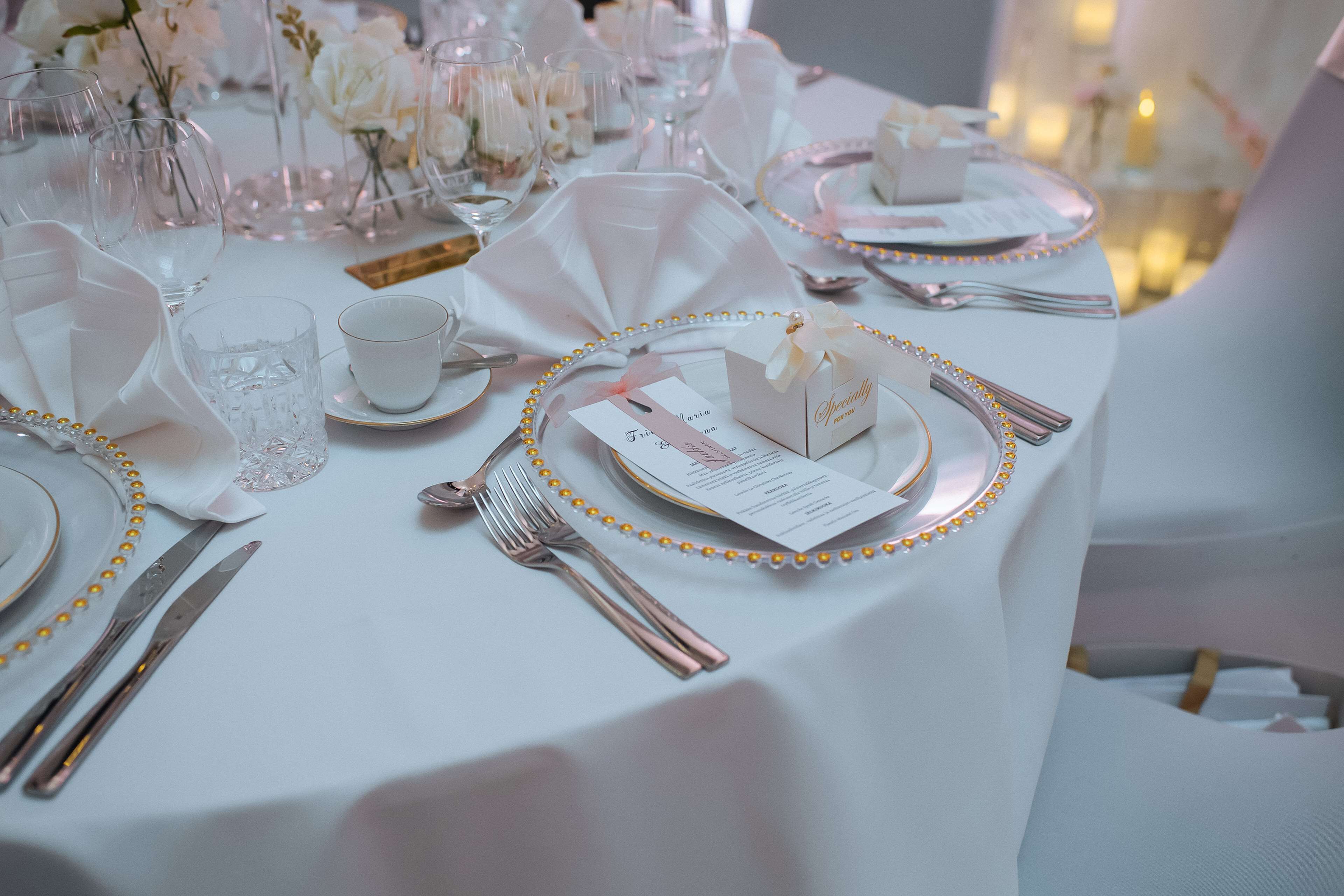 Una mesa dispuesta con manteles blancos, platos con detalles dorados y cubiertos.