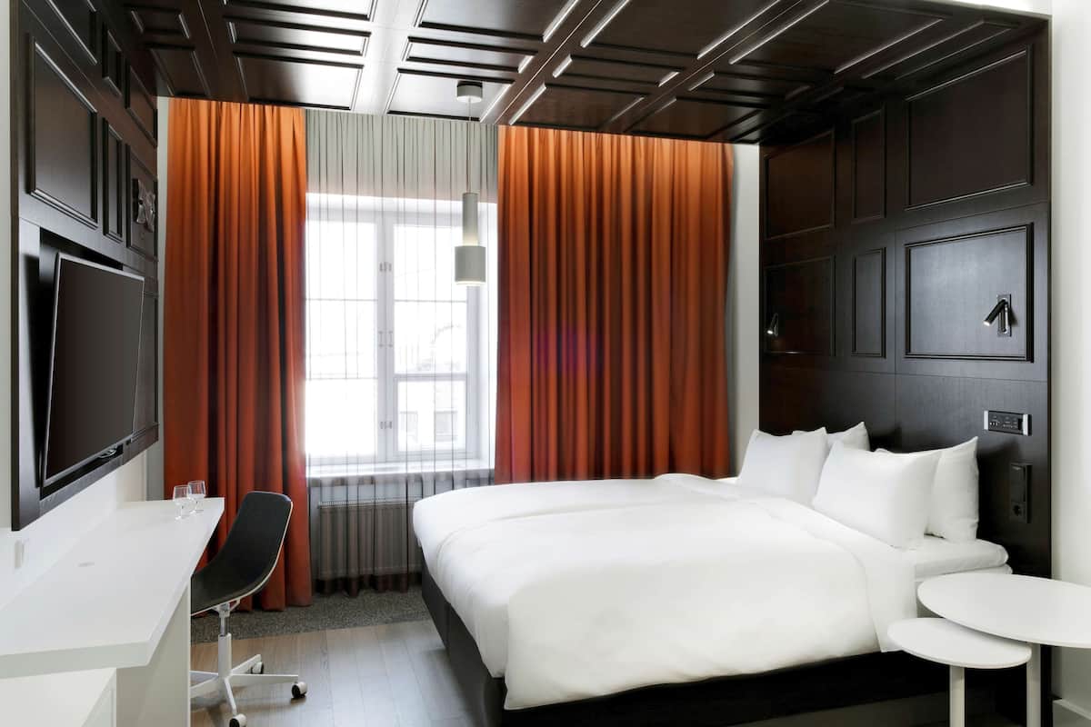 A modern hotel room with a large bed, a desk, and a small table.