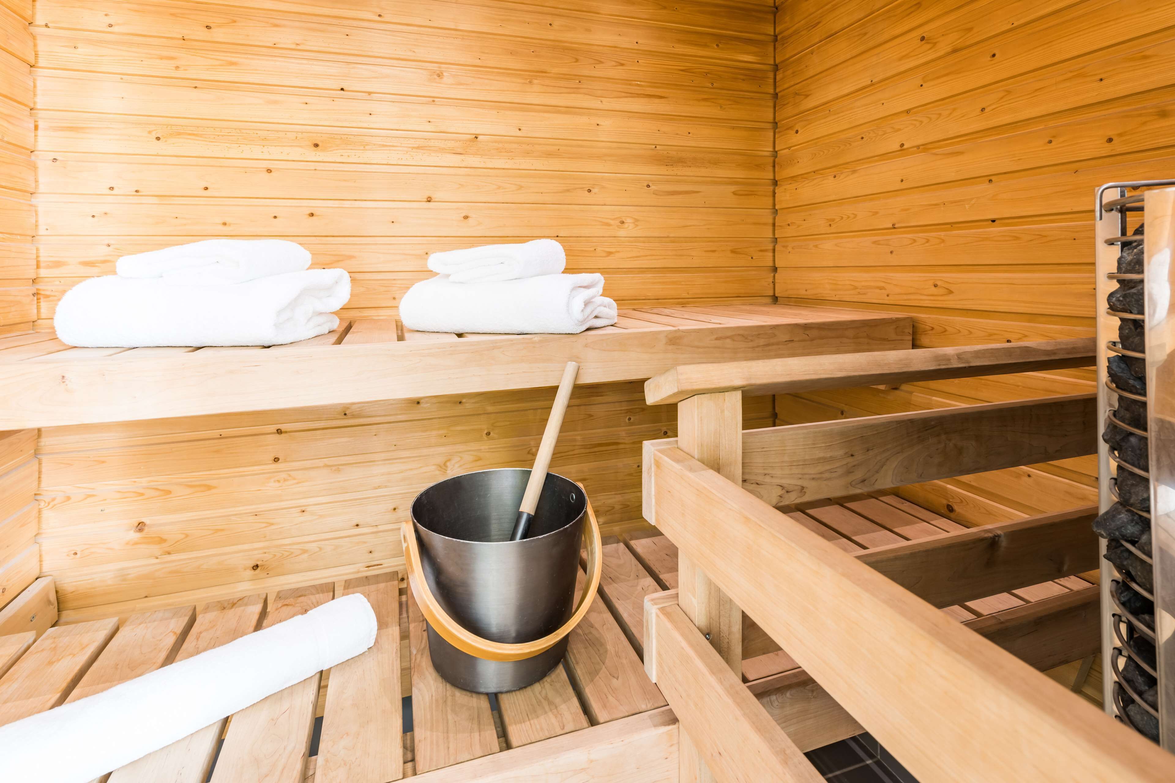 A wooden sauna room with benches, a bucket with a ladle, and stacked towels.