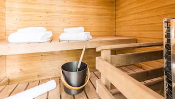 A wooden sauna room with benches, a bucket with a ladle, and stacked towels.