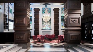Un vestíbulo con suelo de mármol a cuadros, sillas rojas y una ventana de vitral con candelabro.
