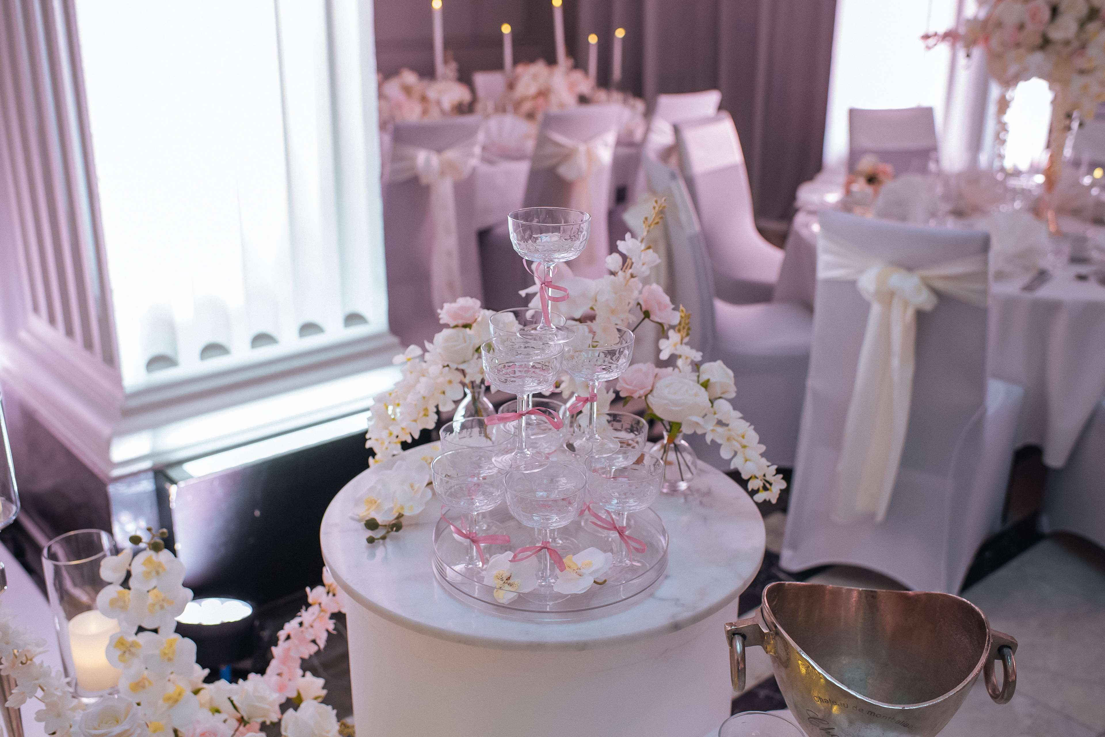 A table set with white chairs, a tiered glass stand, and a copper bucket.