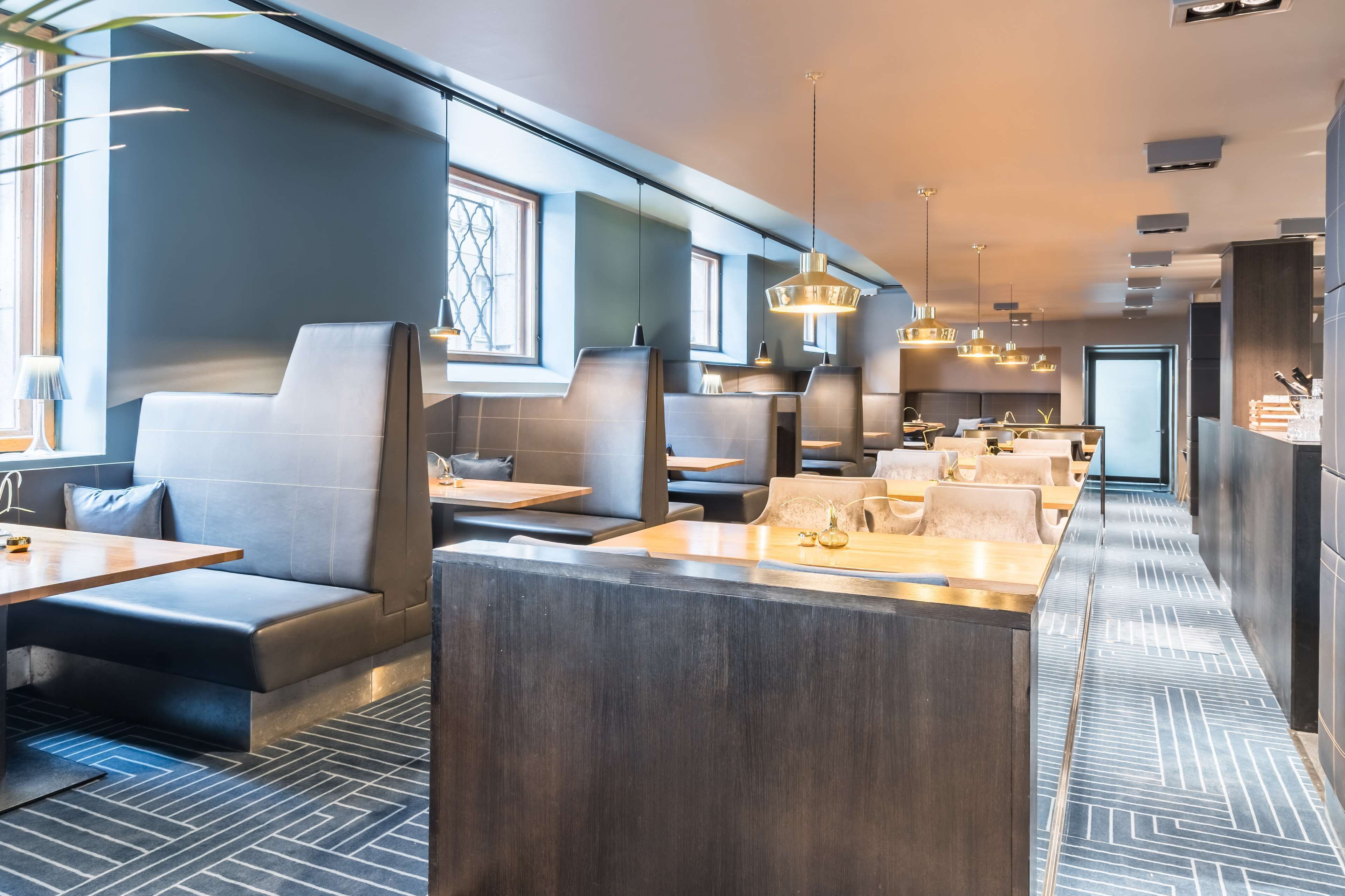 En modern restaurang med höga avskilda bås, långa gemensamma bord och hängande lampor.