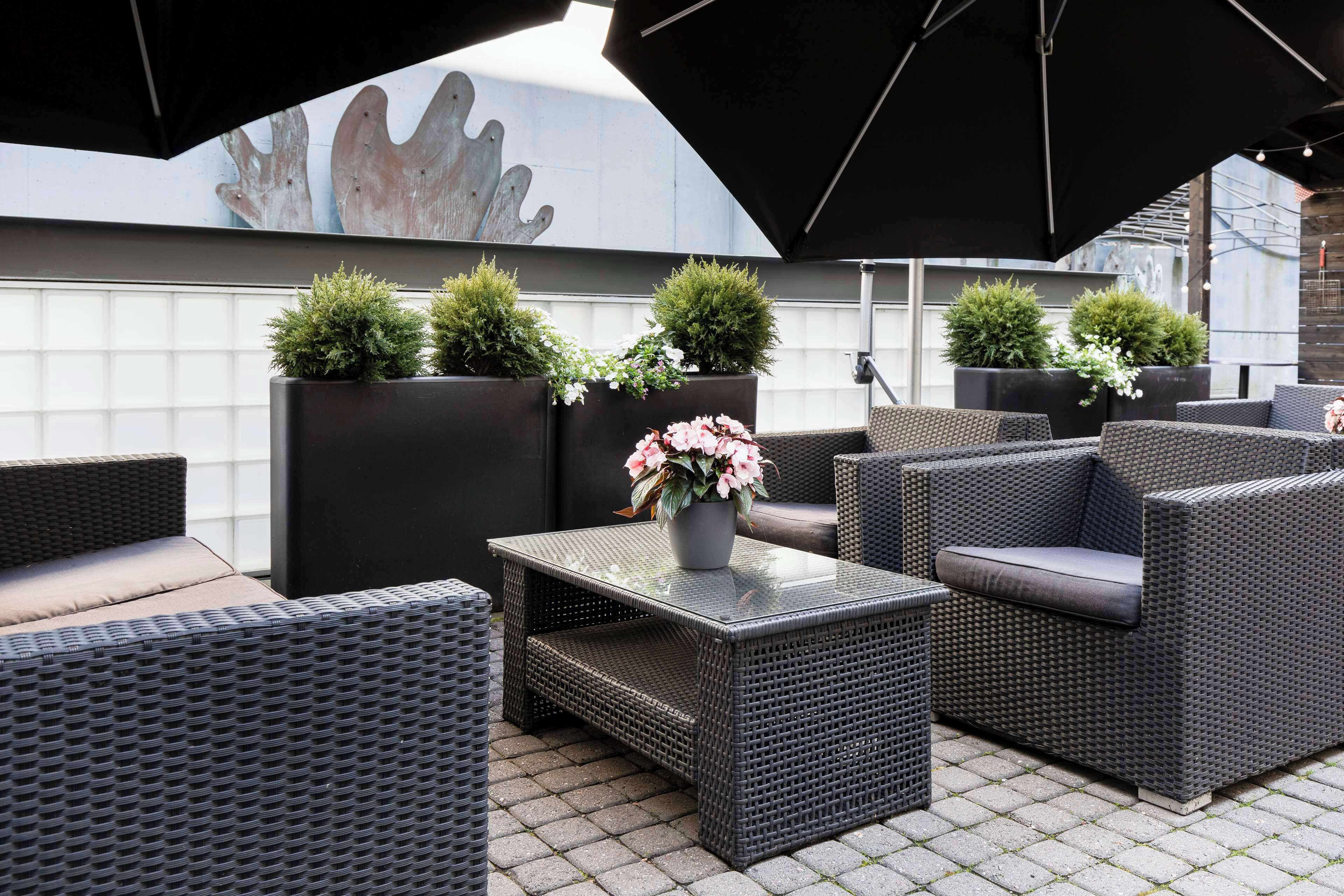 An outdoor seating area with wicker furniture, potted plants, and umbrellas.