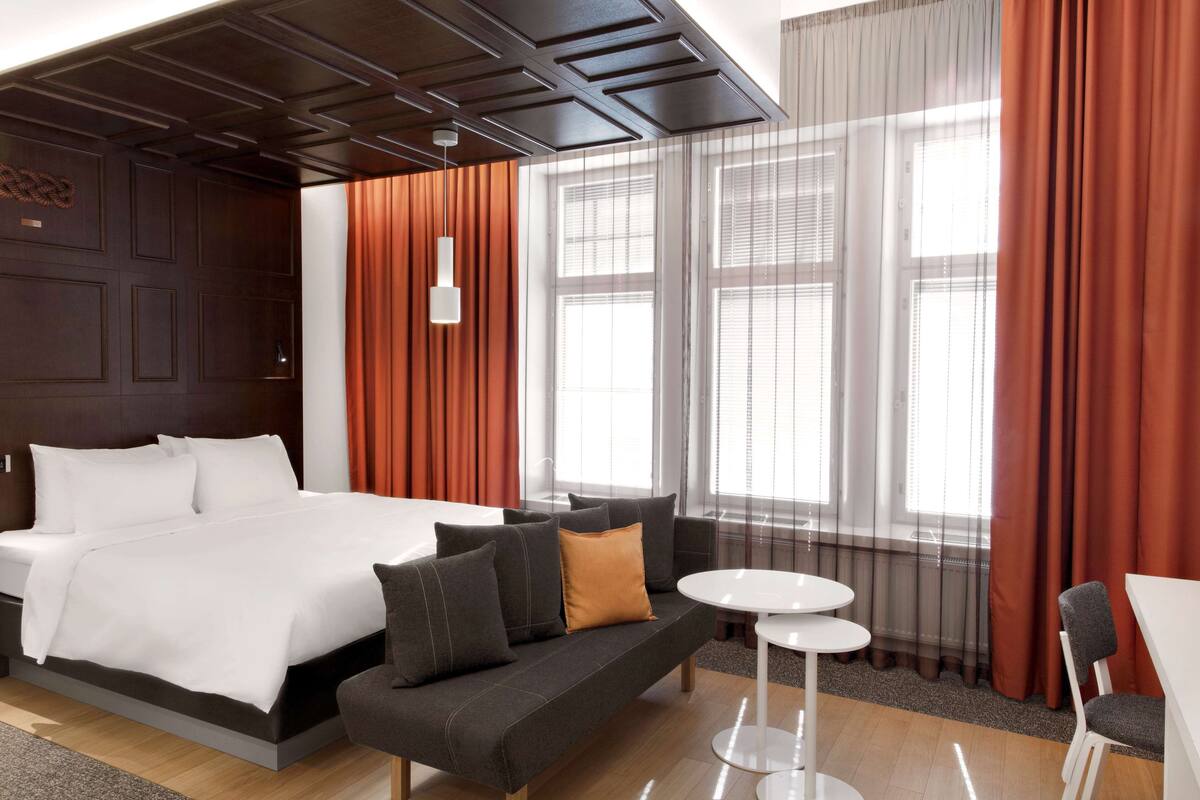 A modern hotel room with a large bed, a sofa, a small table, and a chair.
