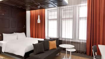 A modern hotel room with a large bed, a sofa, a small table, and a chair.