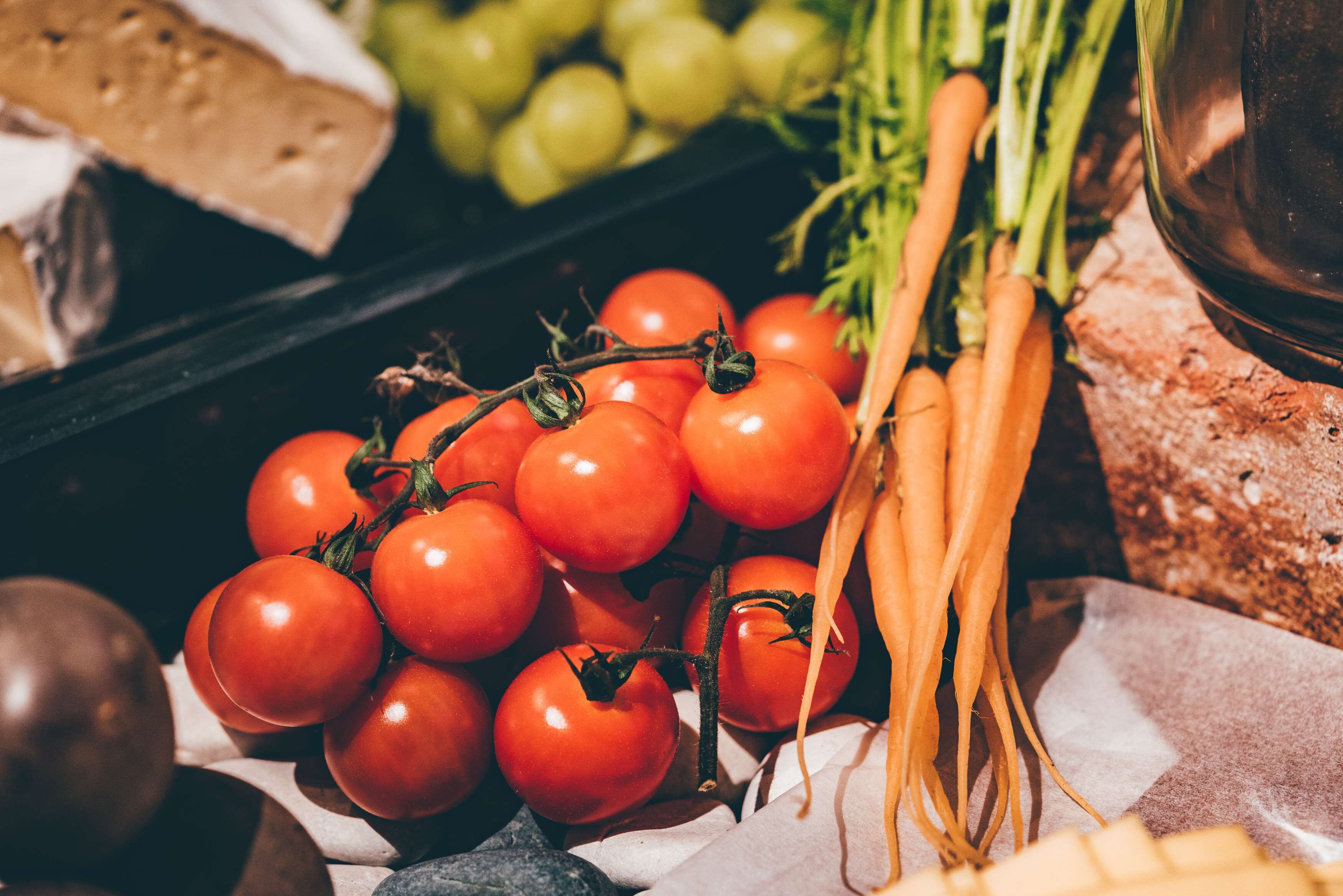A display of fresh produce including tomatoes, carrots, and grapes.