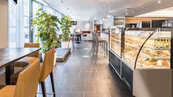 A modern restaurant with a long counter, seating area, and a display case with food items.