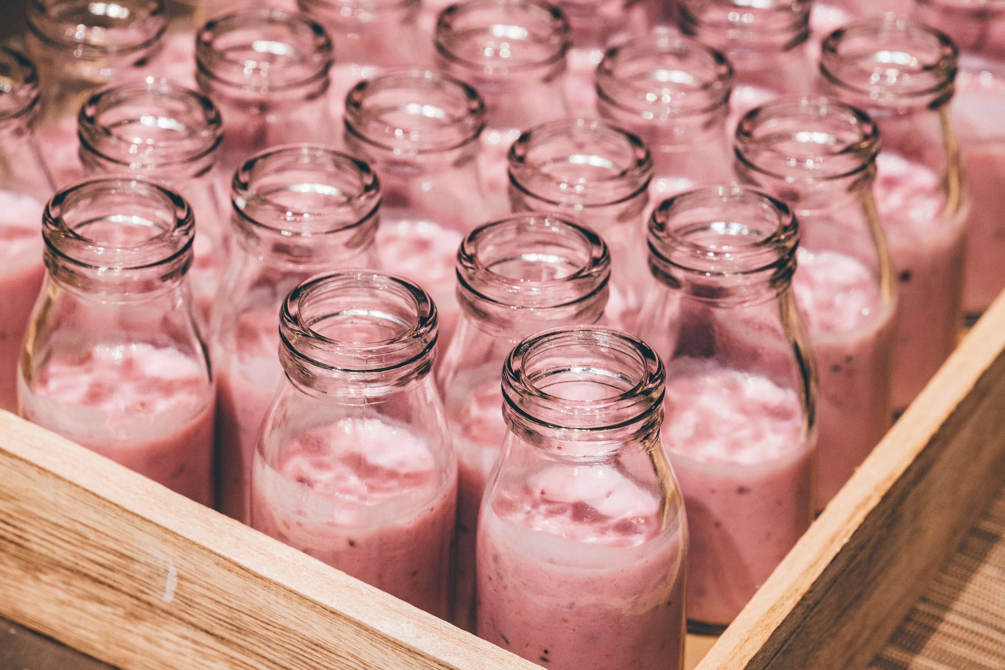 A wooden crate filled with clear glass bottles containing pink smoothies.