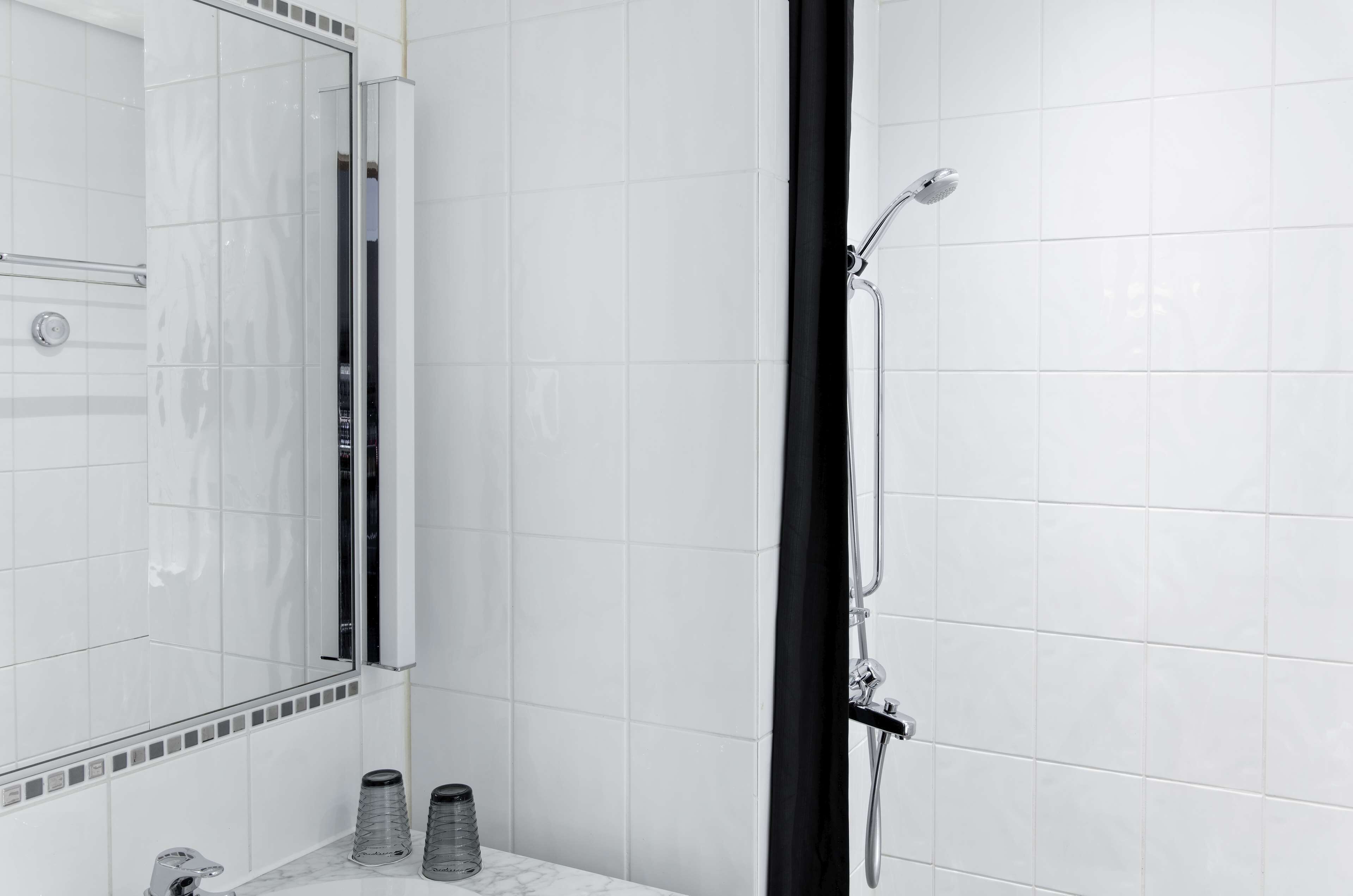 A modern bathroom with white tiles, a glass shower enclosure, and a black shower curtain.