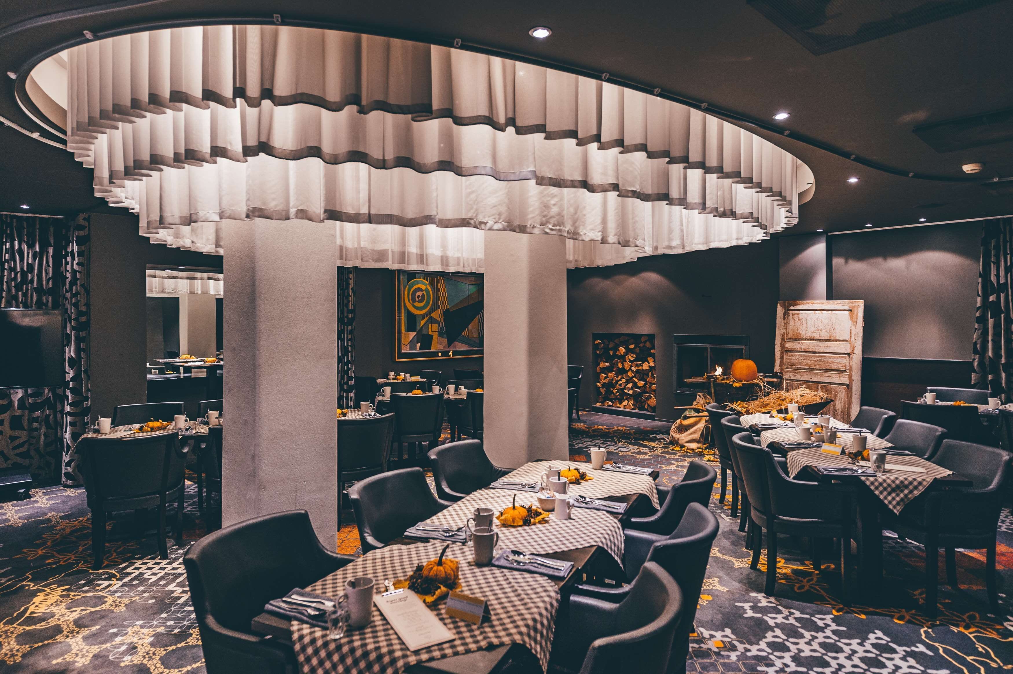 A restaurant with checkered tablecloths, black chairs, and a unique ceiling light fixture.