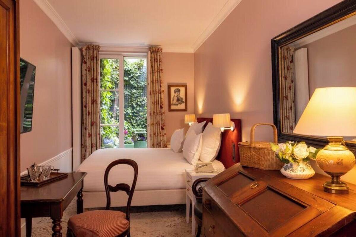 A hotel room with a bed, a desk, a chair, a lamp, and a window with curtains.