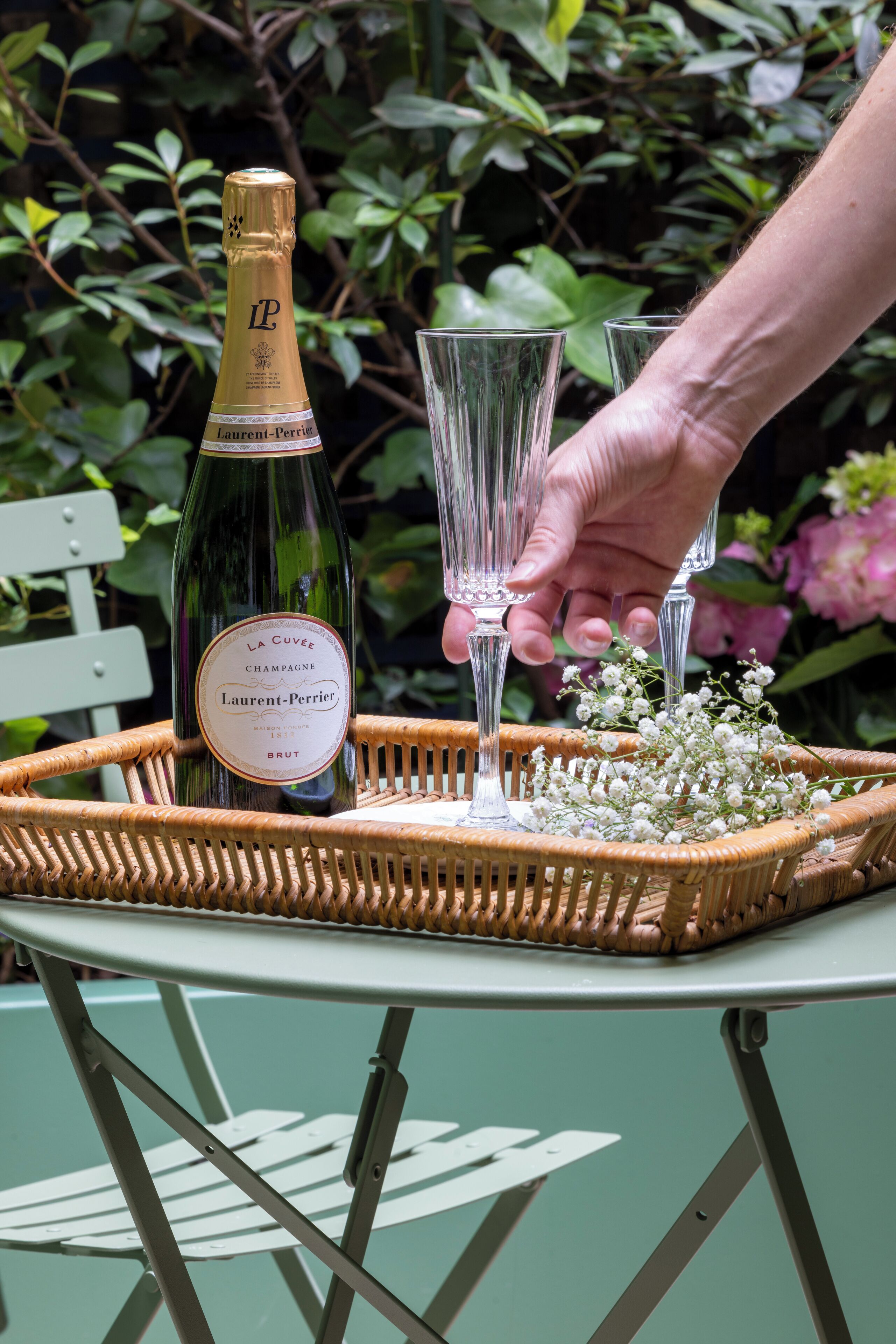 A bottle of champagne and two glasses on a wicker tray on a table.