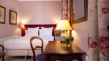 Una habitación de hotel con cama, una mesa de madera, una silla, una lámpara y cortinas con estampado floral.