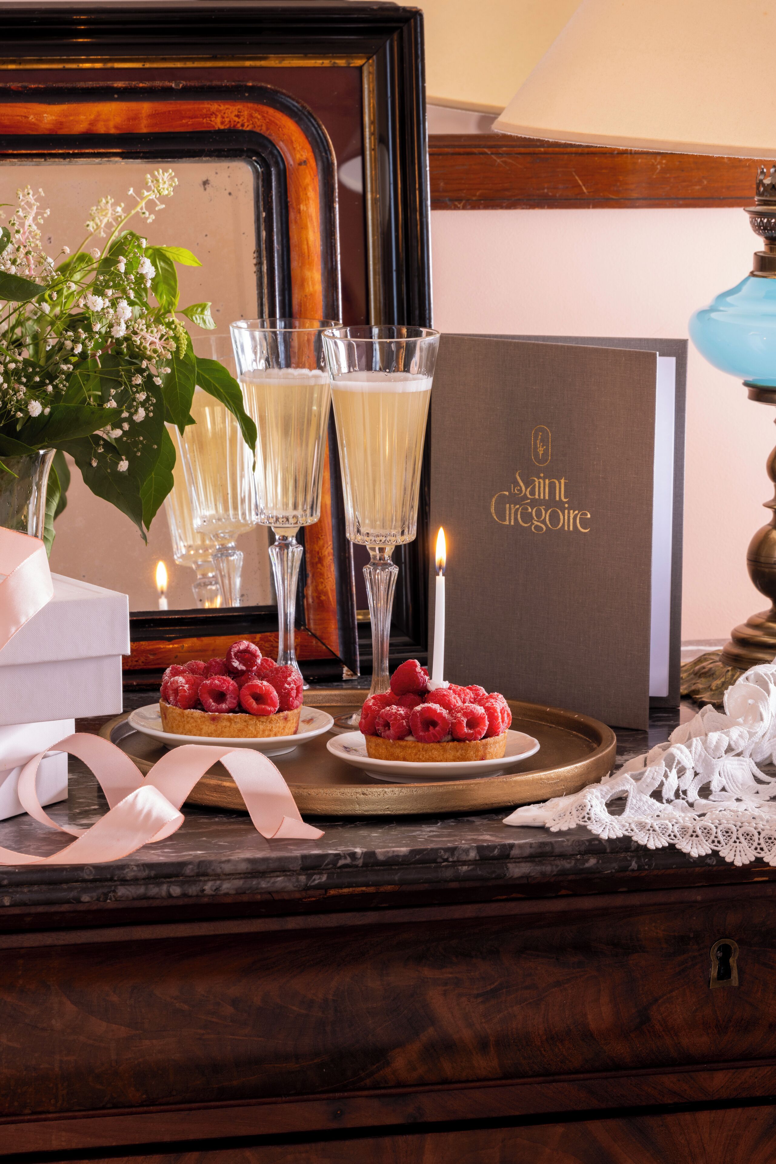 Une table avec des desserts, des coupes de champagne et une bougie, et en arrière-plan, un livre intitulé « Saint Grégoire ».