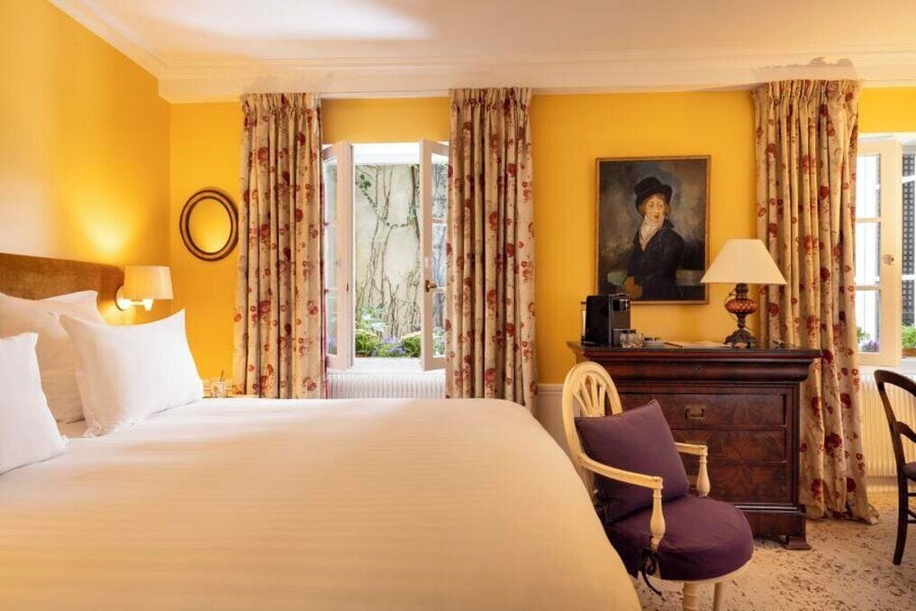 A hotel room with a large bed, a wooden dresser, a chair, and a painting on the wall.