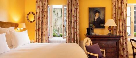 A hotel room with a large bed, a wooden dresser, a chair, and a painting on the wall.