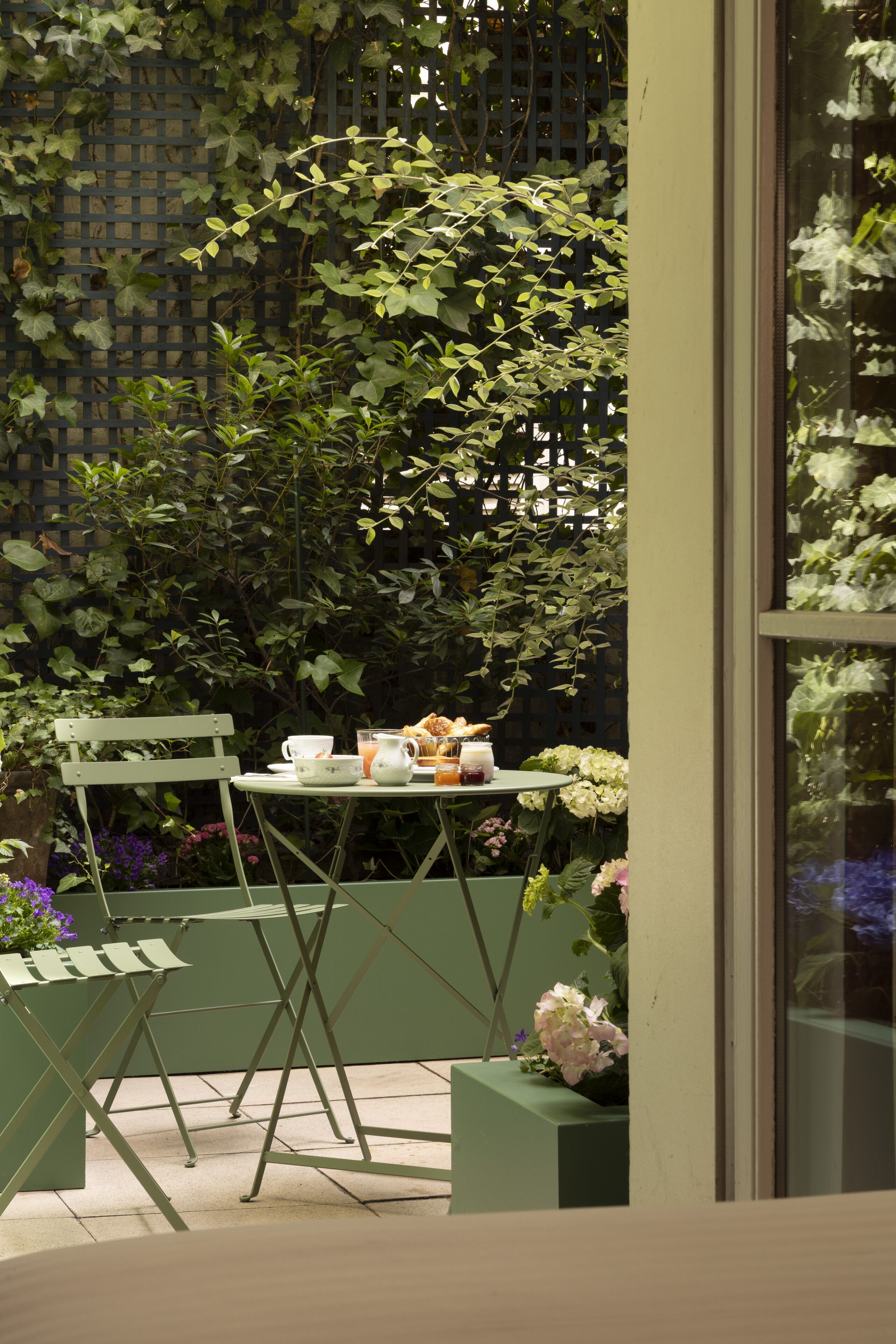 Un petit espace extérieur aménagé avec une table pour deux, entouré de verdure et de fleurs.
