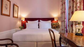 A hotel room with a large bed, two bedside lamps, a wooden nightstand, and a floral curtain.