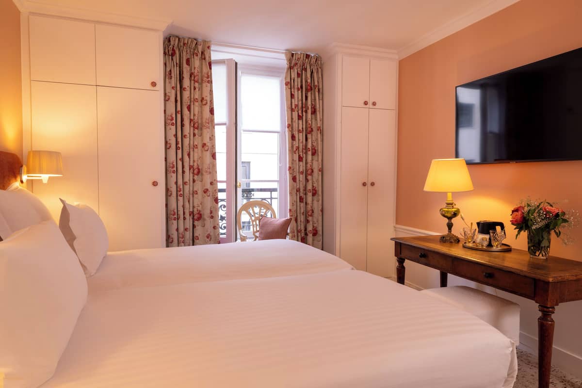 A hotel room with two beds, a TV, a desk with a lamp, and a window with curtains.