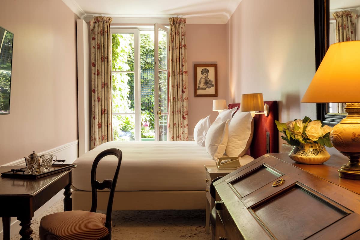 A hotel room with a bed, a desk, a chair, a lamp, and a window with curtains.