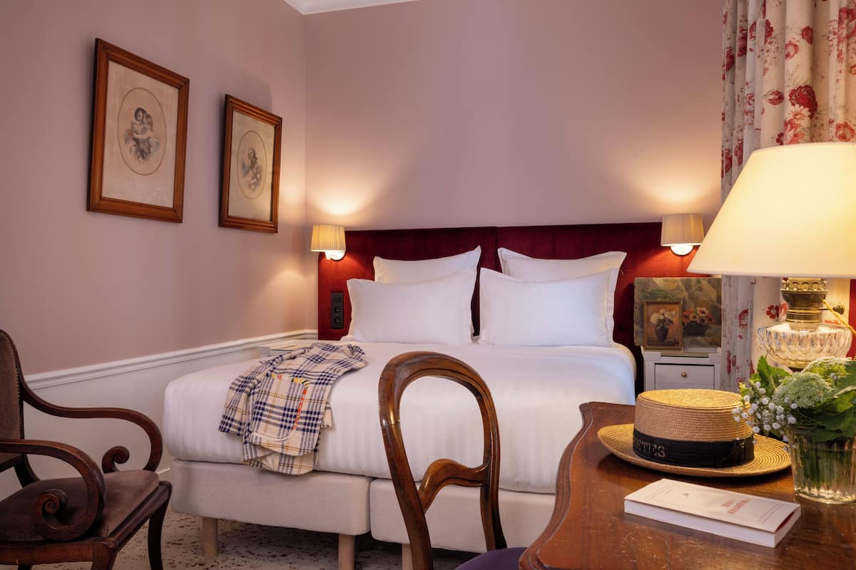 A hotel room with a bed, two bedside tables, a chair, a lamp, and framed pictures on the wall.