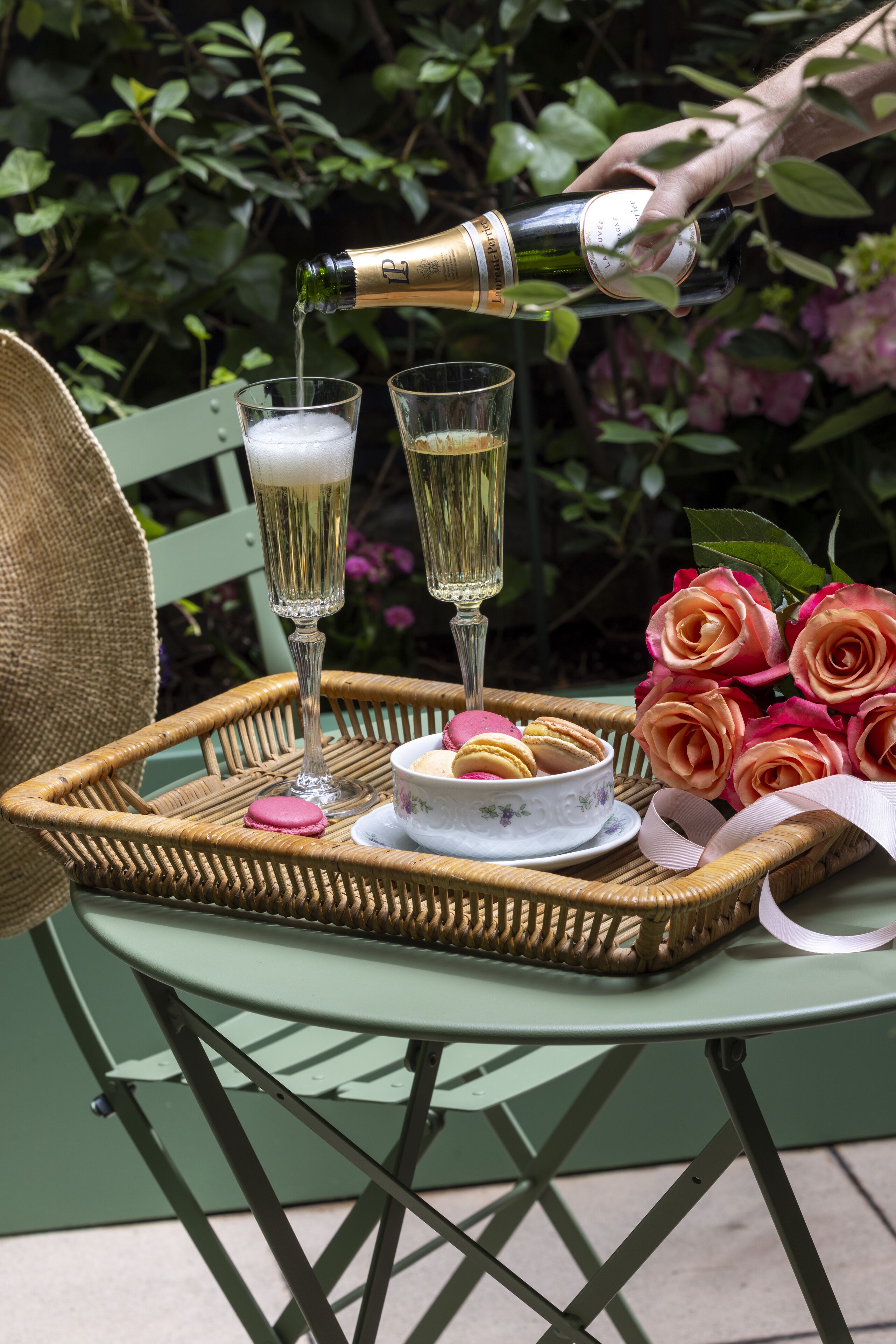 Ett bord med två champagneglas, en korg med macarons och en bukett rosor.