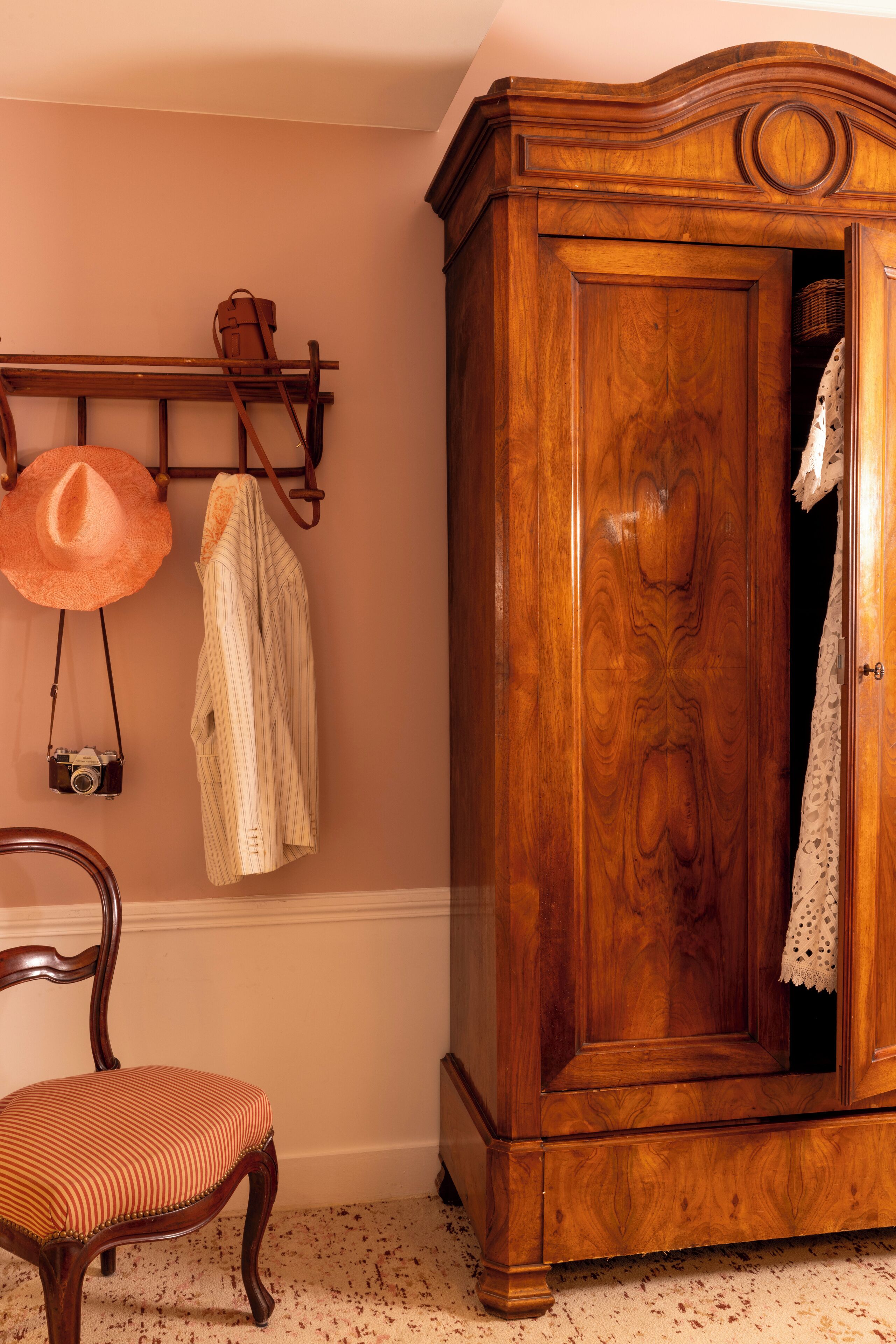 Une armoire en bois avec un miroir, un porte-chapeaux avec des chapeaux, et une chaise avec un coussin à rayures.
