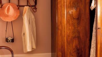 Une armoire en bois avec un miroir, un porte-chapeaux avec des chapeaux, et une chaise avec un coussin à rayures.