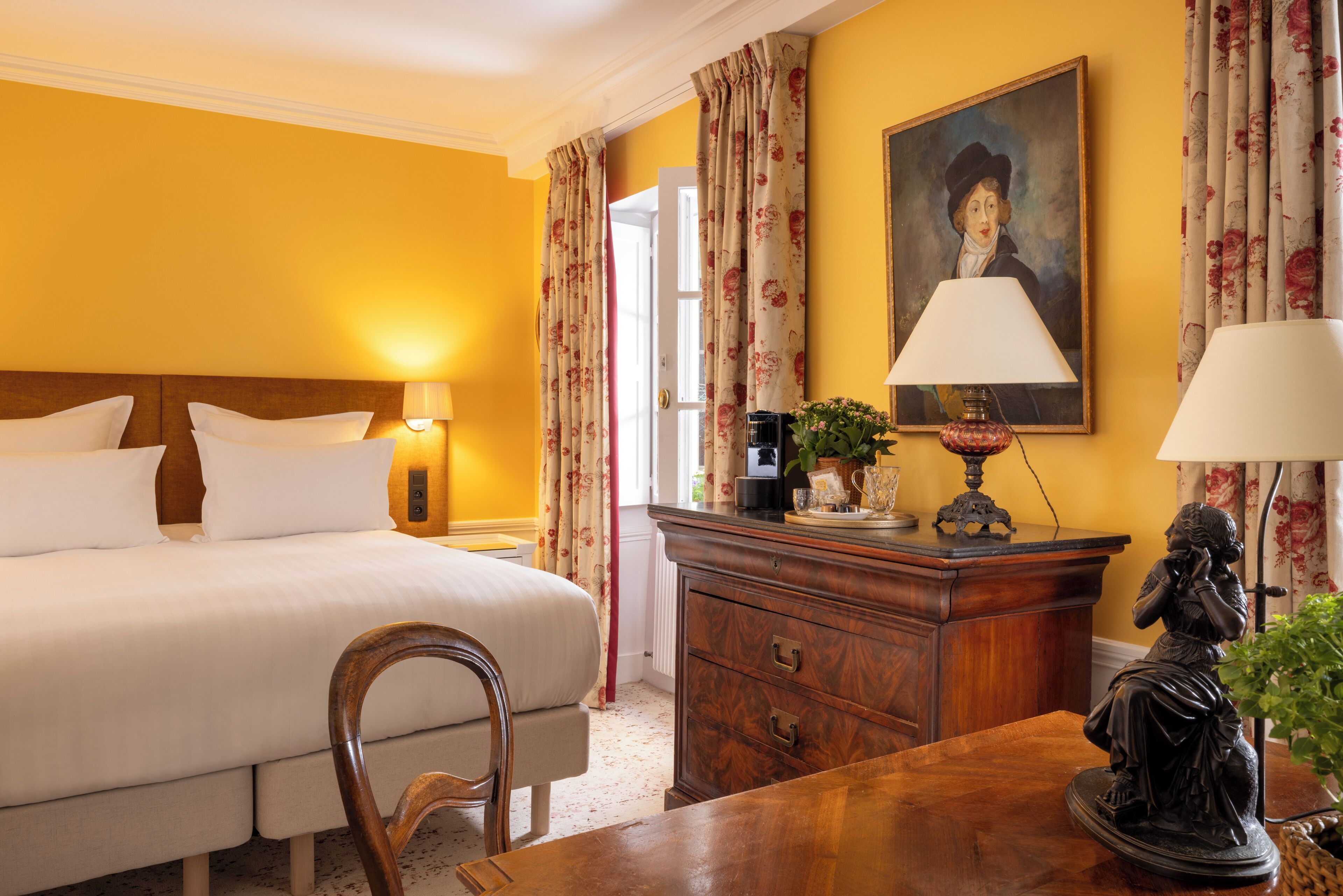 Une chambre d’hôtel avec un lit, une commode en bois, un bureau et une lampe.
