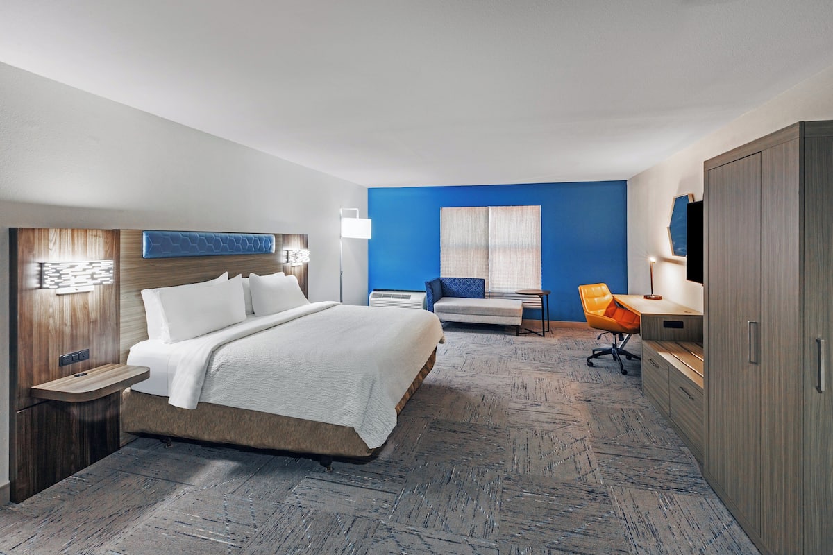 A hotel room with a large bed, a desk, a chair, a TV, and a wardrobe.