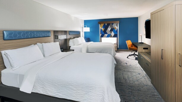 A hotel room with two beds, a desk, a chair, and a wardrobe.