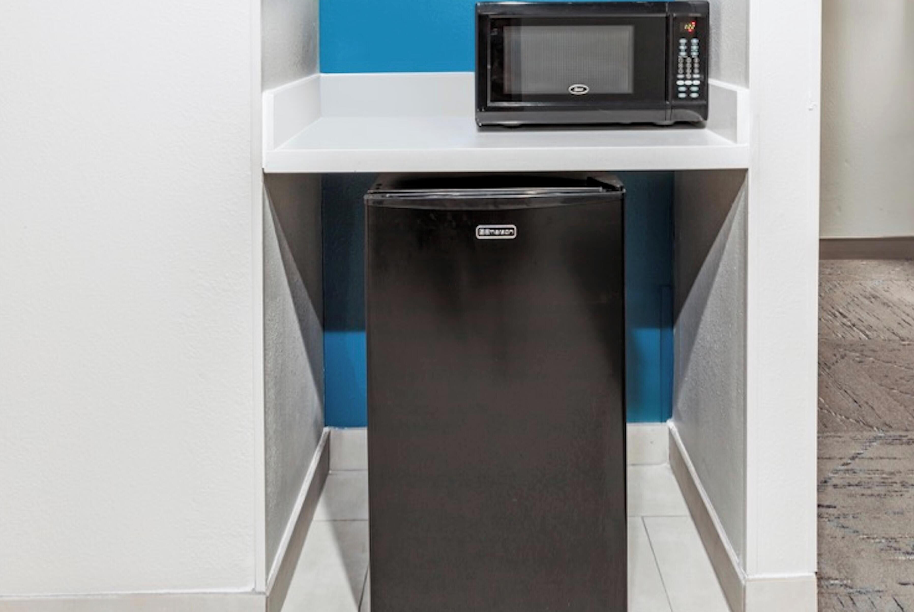 A compact kitchen with a black refrigerator and a microwave on a white shelf.