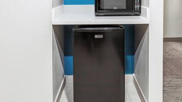 A compact kitchen with a black refrigerator and a microwave on a white shelf.