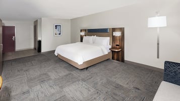 Una habitación de hotel con una cama grande, cabecera de madera, dos mesitas de noche y una lámpara de pared, además de una puerta.