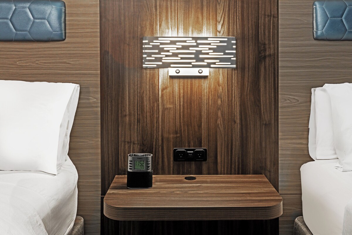 A hotel room with a wooden wall panel, a digital clock, and a power outlet.