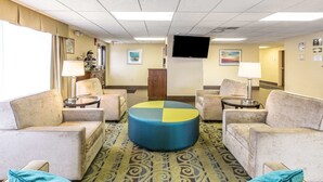 A hotel lobby with a round coffee table, several armchairs, a television mounted on the wall, and a patterned carpet. - Quality Inn Fitzgerald (Fitzgerald)