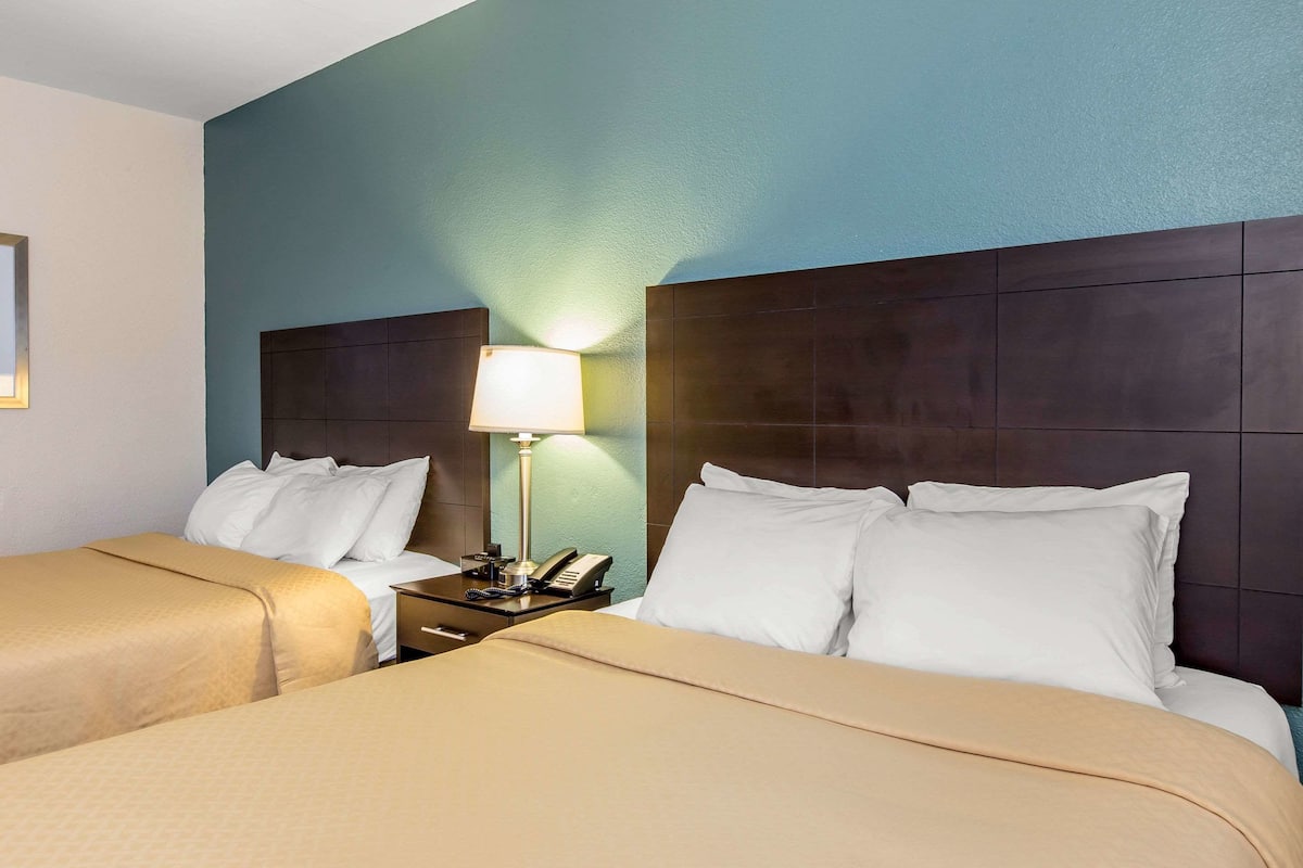 Quarto de hotel com duas camas, uma mesa de cabeceira com abajur e um telefone.