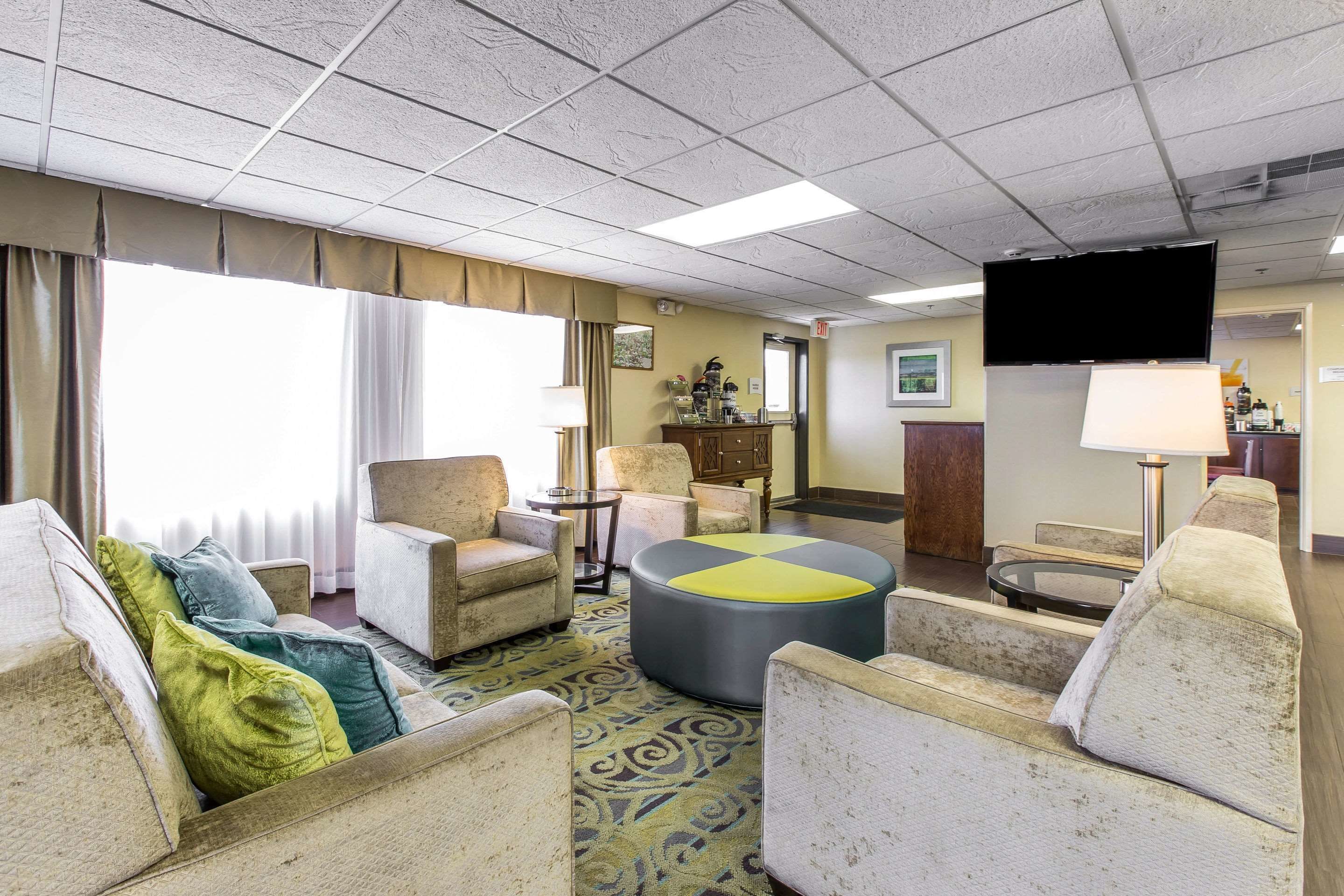 Une chambre d’hôtel dotée d’un coin salon avec des fauteuils et un pouf rond, d’un téléviseur à écran plat fixé au mur et d’une petite table avec une lampe.