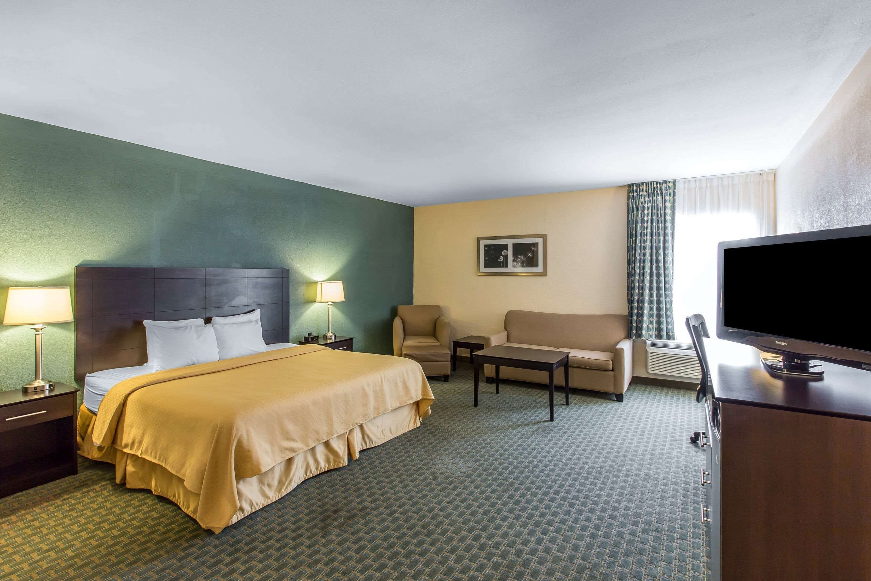 A hotel room with a bed, a desk with a television, a sofa, and a chair.