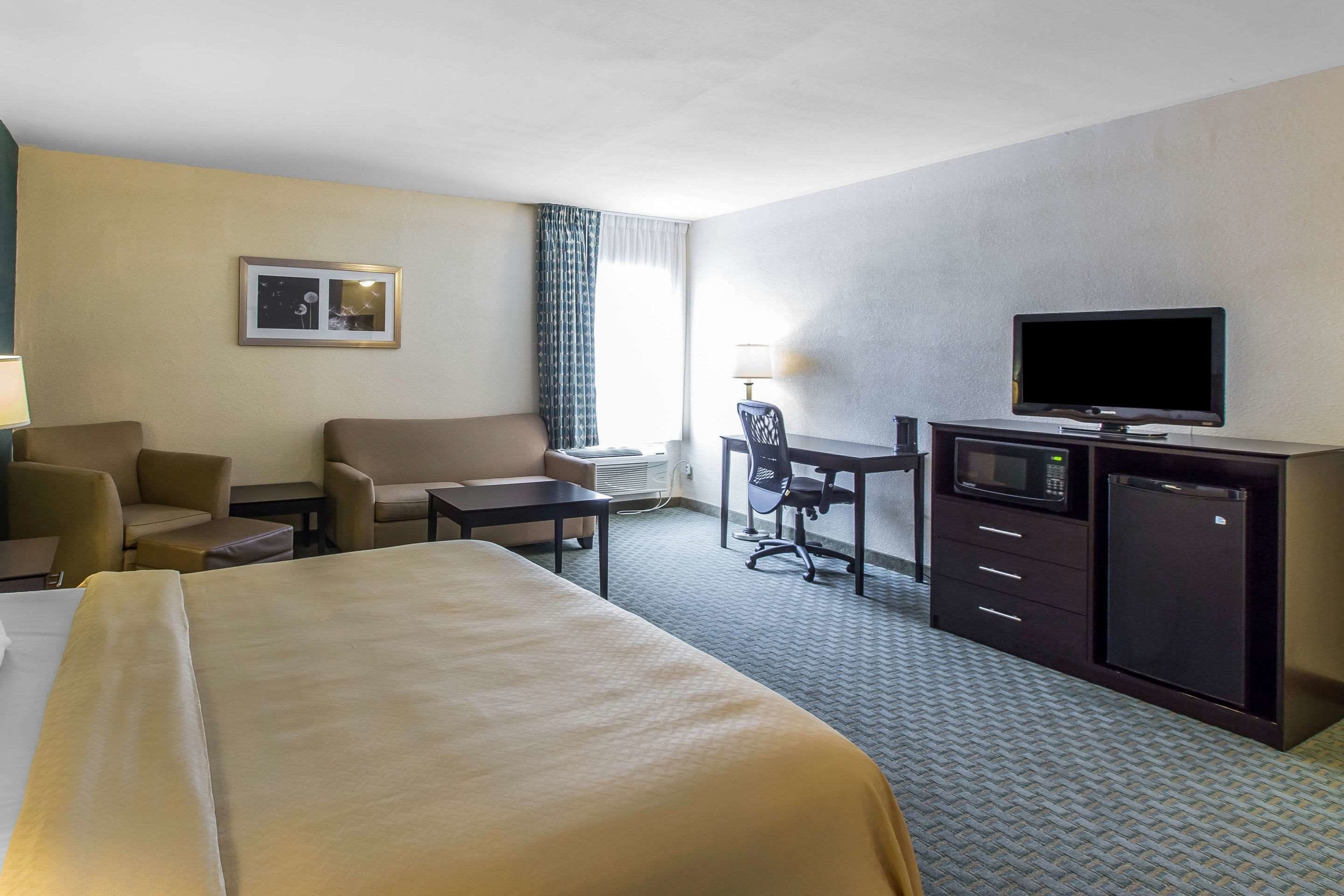 A hotel room with a bed, a desk, a television, a microwave, and a refrigerator.