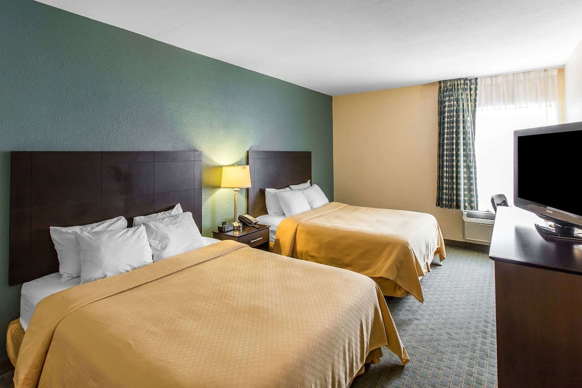 Quarto de hotel com duas camas, uma televisão e uma escrivaninha.