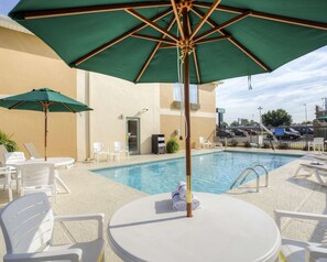 A poolside area with a green umbrella, white lounge chairs, and a small table with towels.