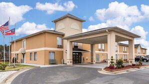 A hotel with a central entrance, a flagpole with an American flag, and a covered parking area. - Quality Inn Fitzgerald (Fitzgerald)